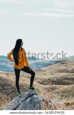 Sports girl in sportswear stands on a stone against the backdrop of mountains