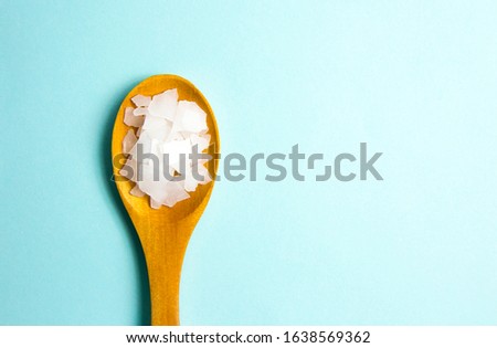 Magnesium Chloride Flakes scattered around brown wooden spoon on blue background. For making foot bath, taking a magnesium-rich bath allows full body exposure to a concentrated solution of magnesium. Royalty-Free Stock Photo #1638569362