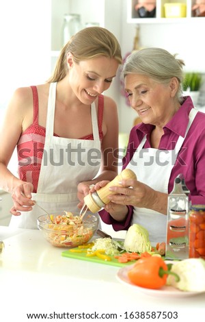 Smiling senior mother and adult daughter cooking together at kitchen