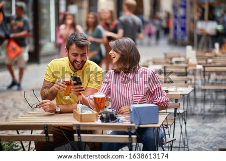 Happy Man and  girl sitting at a cafe drinking beer and looking at pictures on a mobile phone.