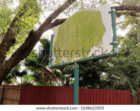 Sign with nothing on it except green blob, red fence and oak trees in background.