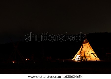 Night photo of the camping site in Japan. Yellow tent with light inside in the darkness. Stars in the sky.
