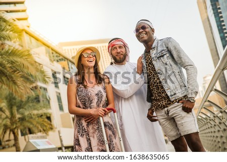 A European woman in a dress and with sunglasses. A man with a beard in an Arabic costume. An African American with sunglasses. Dubai
