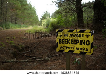 Be aware beekeeping activity ahead yellow and black warning sign beside an unpaved in Riverhead Forest, Kumeu, New Zealand.