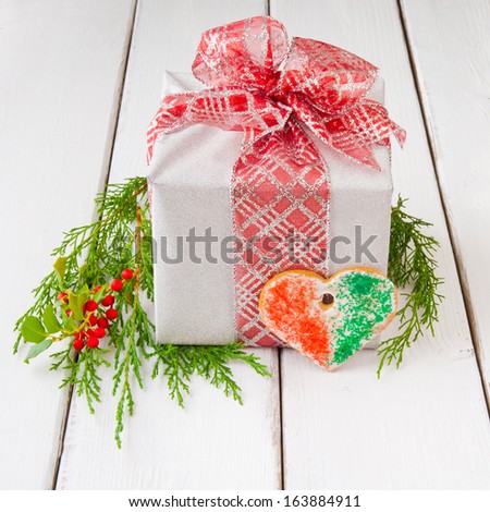 Christmas gift box in silver with red bow with greenery and heart shaped cookie.