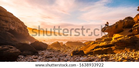 Panoramic of A young girl sitting at the Orange Sunset on the coast of Mount Jaizkibel near San Sebastian, Gipuzkoa. Spain