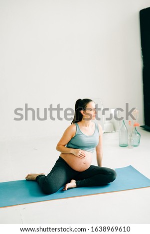 beautiful pregnant girl in sportswear sitting on a yoga Mat and stroking her belly on a studio