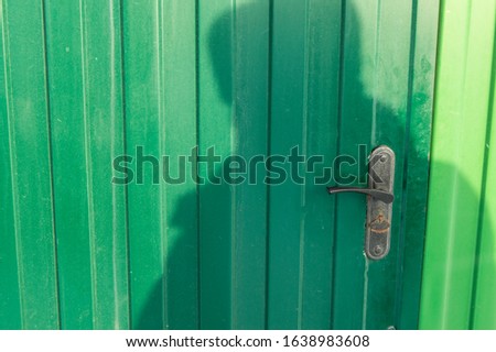 Green metal door made of siding with the shadow of a human silhouette. Abstract background