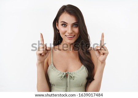 Confident and assertive pretty brunette woman inviting check-out promo, recommend website, showing company banner, smiling camera, pointing finger up to advertise product link