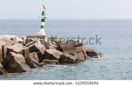 Green and white striped beacon tower standing on the entrance breakwater of Marina da Calheta. Madeira, Portugal