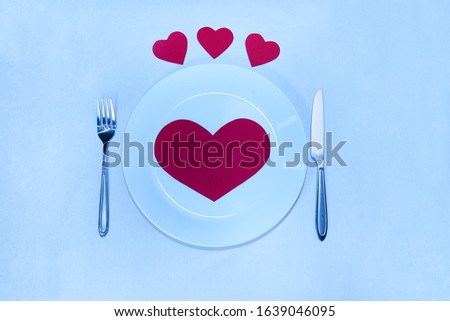 Big red heart made of paper on a white plate and small hearts with a knife and a fork for Valentine's Day                           