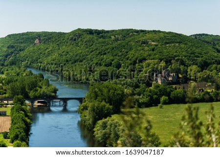 View of Dordogne river in Dordogne valley with Castelnaud-la-Chapelle Castle in right side of picture and old stone bridge in summer day. Travel tourist destination Aquitaine, France.