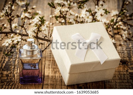 Gift box and bottle of perfume with branches of flowering cherry tree on the wooden background. Concept of giving a gift on holidays.