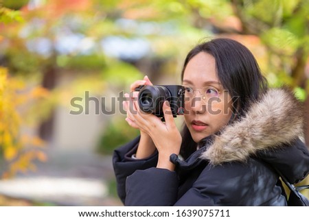 Young beautiful photographer with the professional camera taking photo beautiful autumn colourful maple leaf in Kyoto Japan.