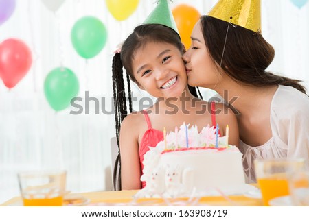 Copy-spaced image of a young mother kissing her b-day daughter on the foreground