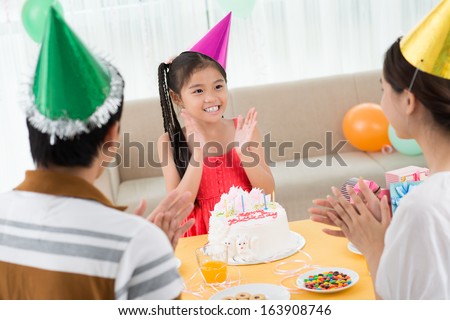 Image of a cheerful b0day girl clapping hands with her parents on the foreground