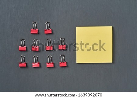 Rows of red metal binders near blank square paper for note lies on dark concrete desk in office, school or home. Space for text. Top view