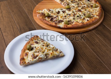 Delicious piece of pizza served on the plate. Meat pizza on wooden board. Made with Mozzarella, picanha meat, onion, cheese, tomato sauce and olives. Filet Steak, meat.