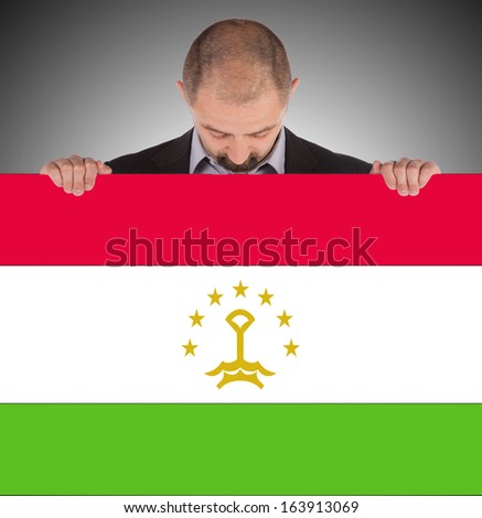 Smiling businessman holding a big card, flag of Tajikistan