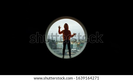 Girl up high in building standing and looking out from a circular window.