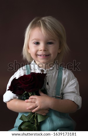 Beautiful toddler boy, holding red roses as present for mother's day