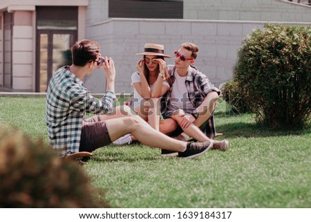A Young Guy Takes Pictures With His Phone A Couple Of Friends. Students In Sunglasses Relax And Take Pictures In Nature.