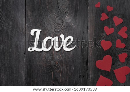 white lettering Love on a rustic background with red cardboard hearts on the side. with place for text