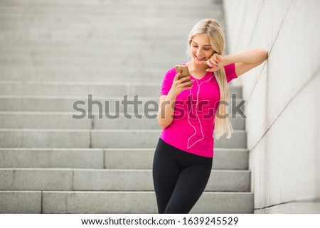 beautiful young woman in sportswear in the summer on the street in headphones with a phone in her hands