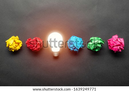 Lightbulb and crumpled colorful paper balls on black background. Successful solution of problem. Idea generation and brainstorming. Genius idea among failing ideas metaphor. Business motivation Royalty-Free Stock Photo #1639249771