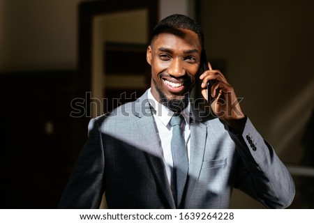 Close up portrait of a happy smiling young man in business suit holding cell phone, talking and looking at camera