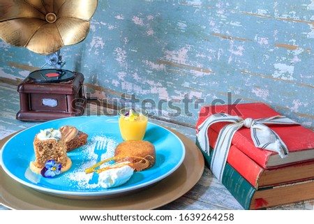Chocolate brownie, malva pudding, pumpkin spice cake with glazed frosting and lemon curd in a small glass on a blue plate with icing sugar decoration, old grammar phone and antique books