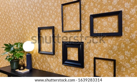 Yellow wall with floral pattern and decorated with empty black frames above a side table