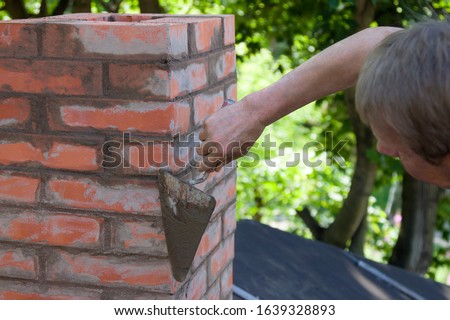 A man making masonry works, working with a trowel and making a chimney of red bricks Royalty-Free Stock Photo #1639328893