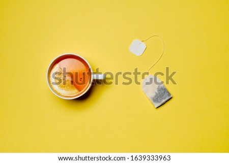 The concept of brewing tea from a tea bag. A cup of tea with lemon on a yellow background. Close up.