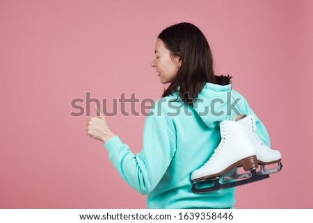 Figure skating for adults, Hobbies and a healthy lifestyle. A young woman in a bright sweatshirt with figure skates on her shoulder, a Studio shot on a pink background.