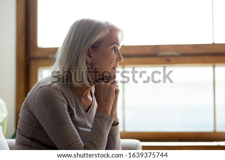 Side view of sad thoughtful middle-aged mature woman sit on couch at home look in window distance mourning, upset pensive senior female lost in thoughts thinking or pondering over past Royalty-Free Stock Photo #1639375744