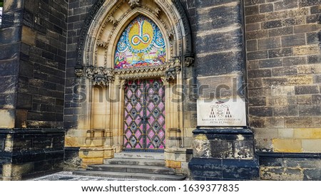 The picture shows the colorful door and a sign right next to it. It belongs to the Cathedral of St. Paul and St. Peter in the south of Prague.