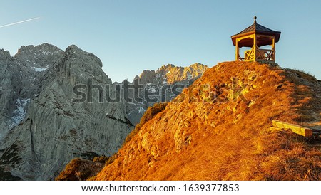 The picture shows a small wooden pavilion on the peak of a mountain which is touched by the morning sun while the background remains shady.