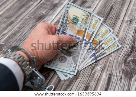 A man's hand in handcuffs and US dollars banknotes on wooden table. Corruption or economic crime concept.