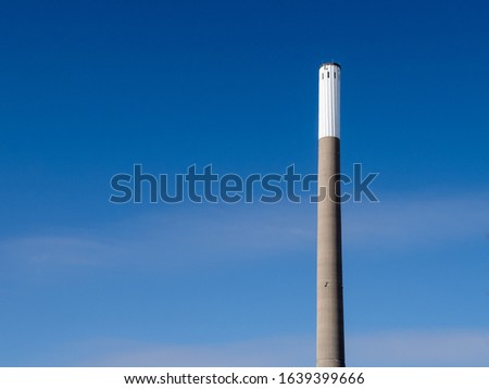 an old tall concrete industrial chimney or smokestack on a clear blue sky