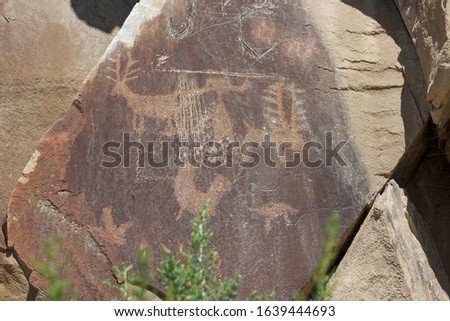 Ancient petroglyphs of animals and a man like figure are carved into sandstone rocks along with some more modern graffiti at Legend Rock State Petroglyph Site in Wyoming.
