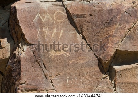 Modern graffiti that is over a hundred years old on a sandstone rock with a small petroglyph carving that is thousands of years old.