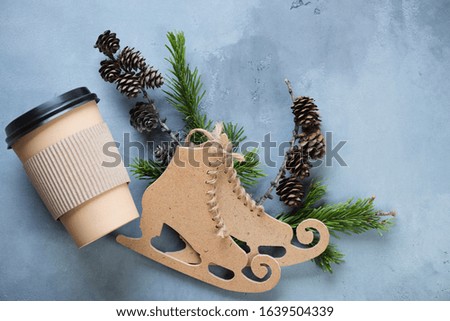 Grey concrete background with decorative skates, fir-tree branches and a takeaway coffee cup, horizontal shot, above view