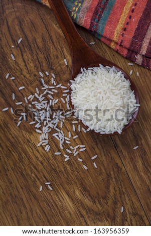 White rice grains in wooden spoon on wood background