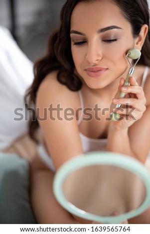 Attractive young woman massaging cheek with massage roller stock photo