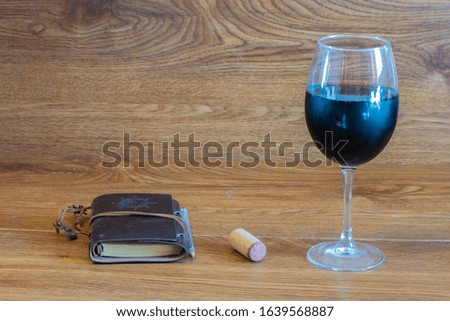 composition of red wine glass on stage of oak tables with a bottle cork and a newspaper accompanied by pencil