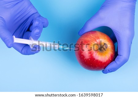 Injection into an apple. A hand in a medical glove with a syringe on a blue background. Genetic modified foods. Injection of GMOs.
