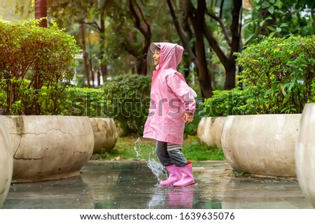 Little asian girl wearing pink rain boots and walking during sleet jumping in a puddle