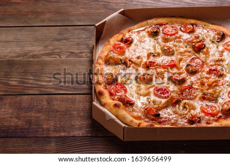 Seafood Italian pizza with shrimp, squid, mussels, fresh herbs and mozzarella on a
dark background. Tasty sliced pizza with seafood and tomato on a concrete background