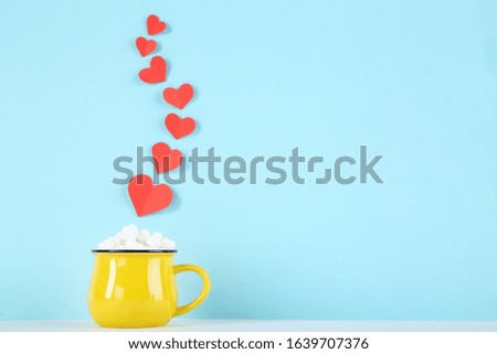 Paper hearts and yellow mug with marshmallows on blue background